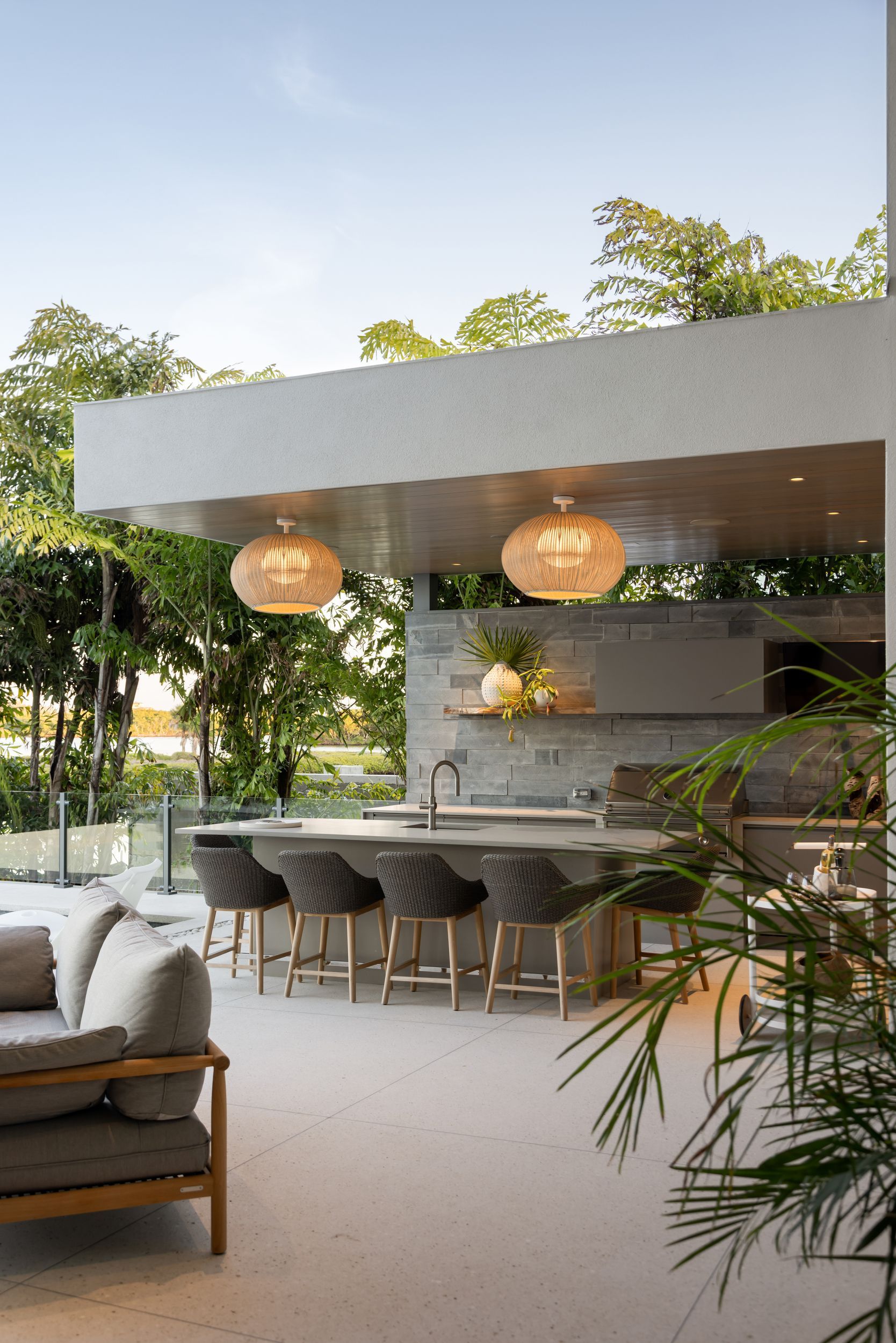 Outdoor kitchen with concrete countertops, bar stools, and wicker pendant lights.