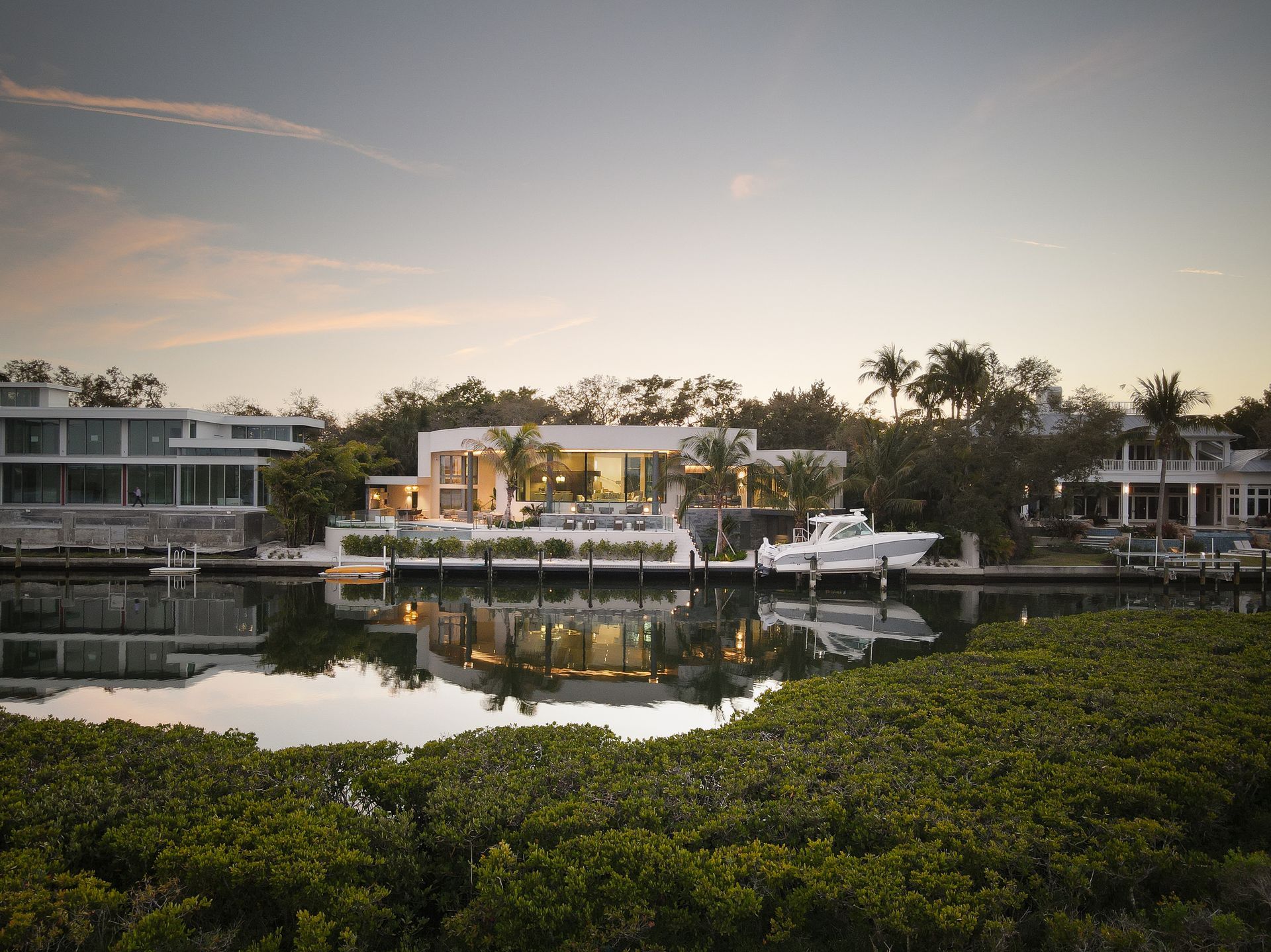 Waterfront home with white exterior, boat dock, and canal at dusk.