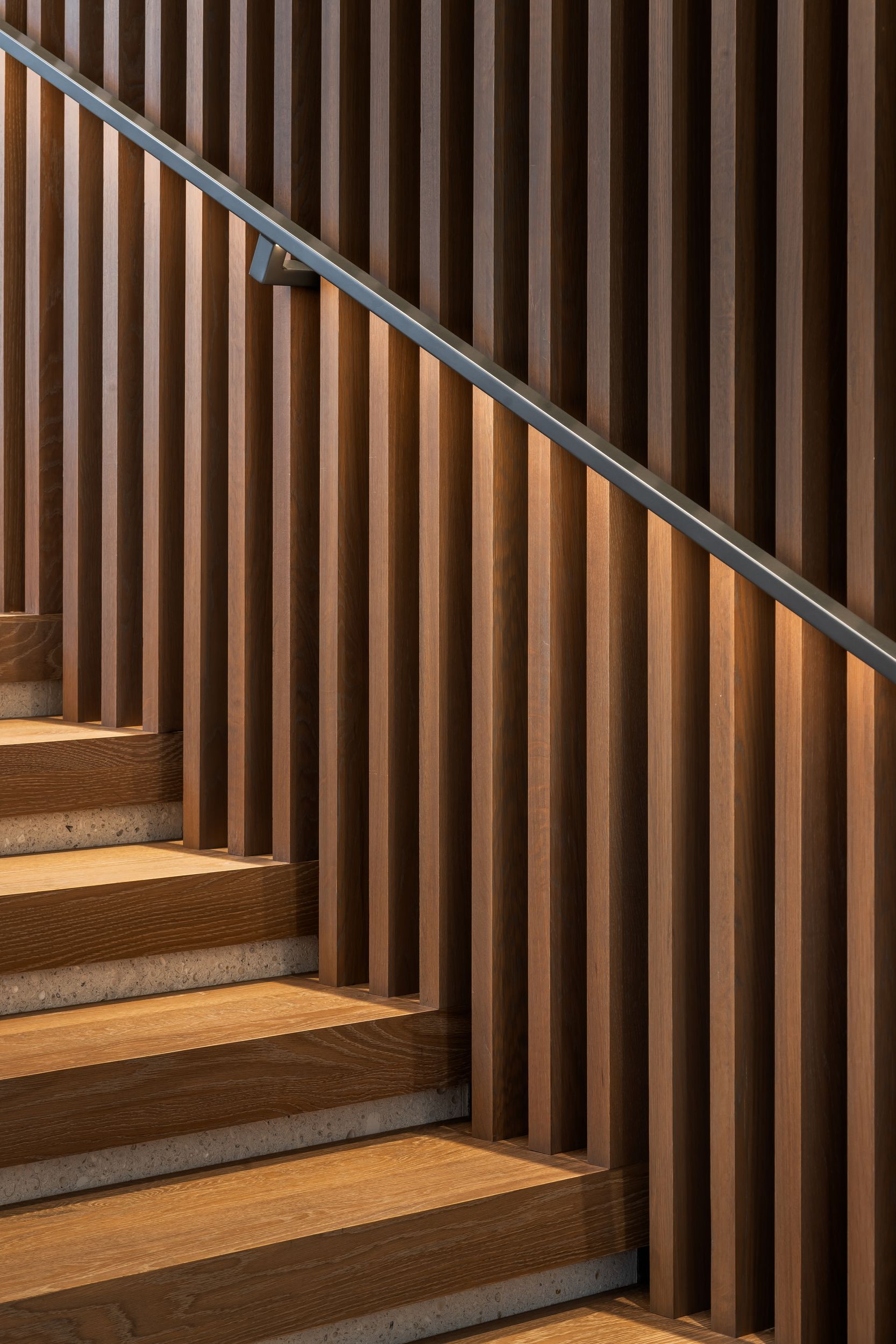 Wooden staircase with vertical slat wall and metal handrail.