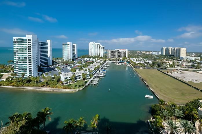 Aerial view of a marina with white high-rise buildings, boats, and clear blue sky.