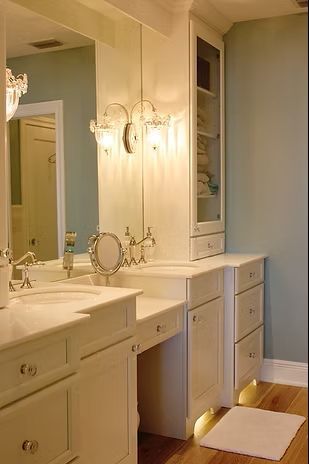 White bathroom vanity with sinks, mirror, lights, and storage cabinet; pale blue walls.