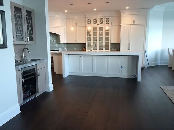 Modern white kitchen with dark wood floors, cabinets, and island. Sink and wine cooler on the left.