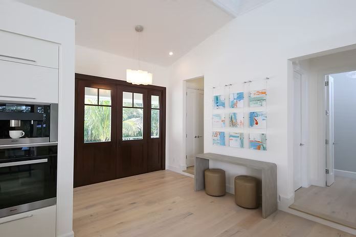 Entryway with dark wood doors, light wood floors, and artwork on a white wall.