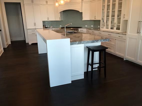 White kitchen with dark wood floors, island, granite countertop, and a black stool.