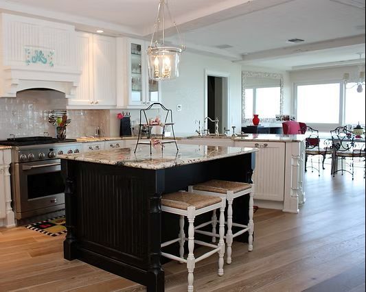 Kitchen with black and white cabinets, island with stools, and light wood floors.