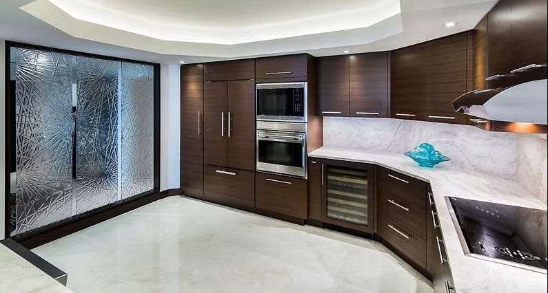 Modern kitchen with dark wood cabinetry, stainless steel appliances, and textured glass wall.