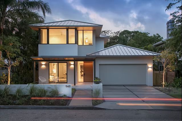 Modern two-story house with a white exterior, gray roof, and a two-car garage. Night setting with lights on inside.