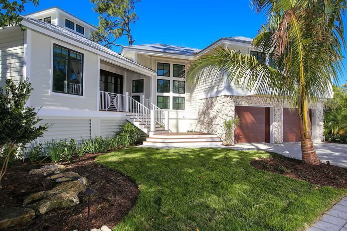 White coastal home with stone accents, brown garage doors, and palm tree.