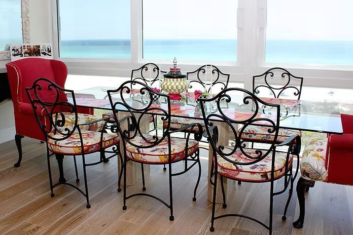 Dining table set with six ornate black metal chairs, red upholstered chair, ocean view.