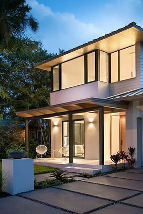 Modern two-story house with illuminated windows and a covered porch, set in a yard with concrete pavers.