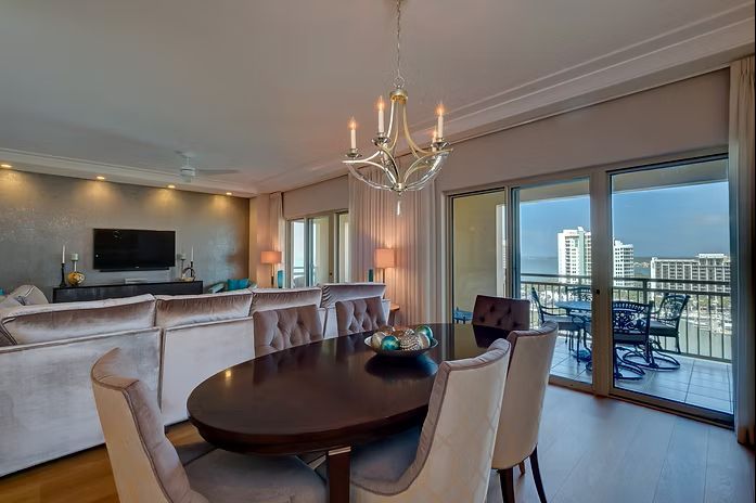Dining room with oval table, chairs, and chandelier; sliding glass door opens to balcony with view.