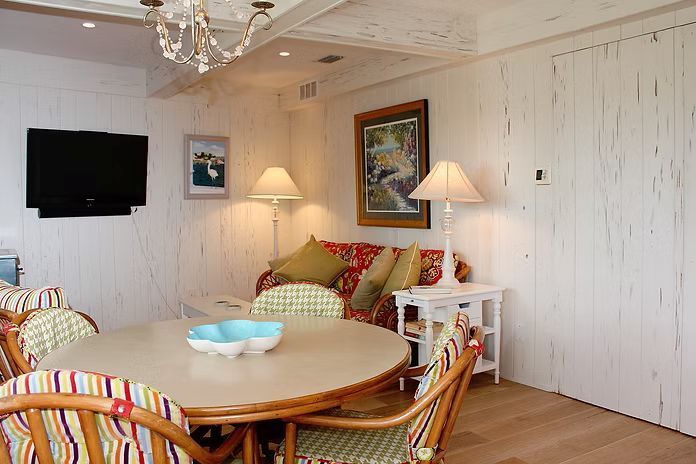 Dining room with a round table, chairs, sofa, TV, and artwork; white paneled walls and wood floor.