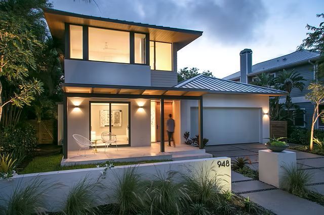 Modern two-story house with a person standing at the entrance.  Grey and white exterior with a garage.