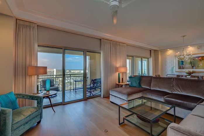 Living room with balcony view, featuring a velvet sectional sofa, turquoise chair, and light wood floors.