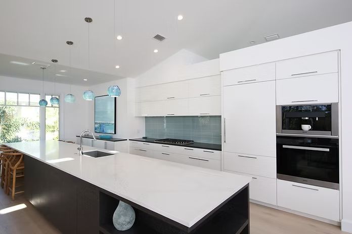 Modern kitchen with white cabinets, dark island, and glass backsplash.
