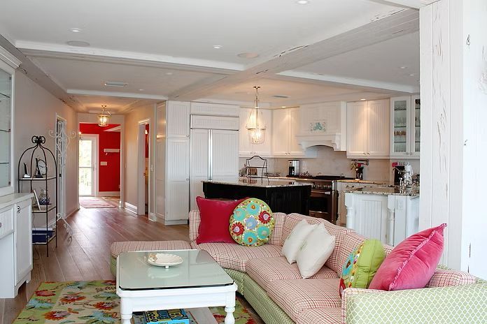 Living room with an open kitchen, pink sofa, and colorful throw pillows.