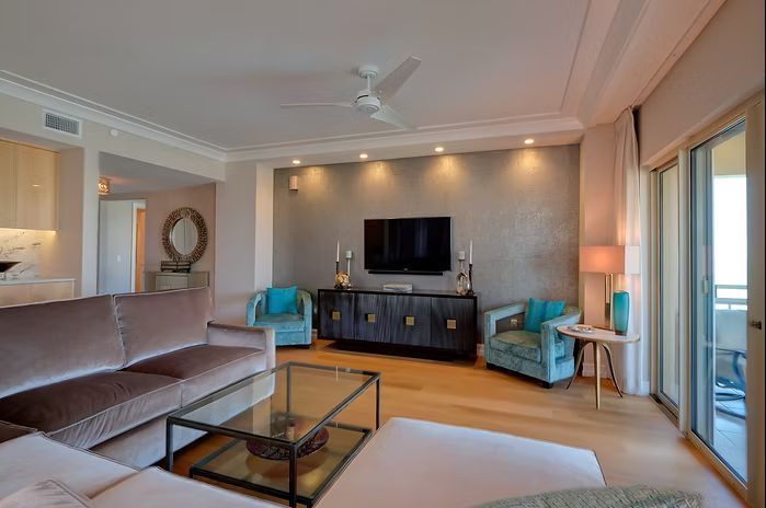 Living room with beige couch, blue armchairs, and a TV mounted on a gray wall.