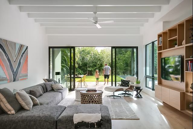 Modern living room with open doors to a backyard; sectional sofa, built-in shelves, and a view of people outside.