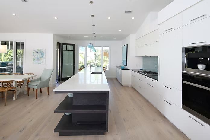 Modern white kitchen with island, cabinets, dining area, and door to a patio.