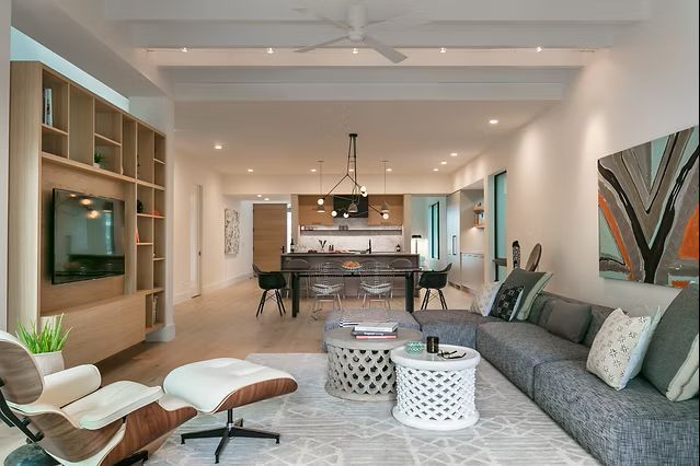 Modern living room with open layout, wood accents, and gray sofa. Kitchen in background.
