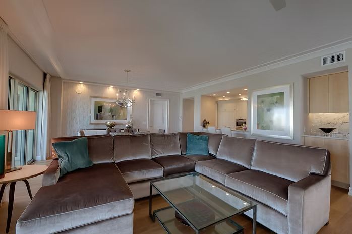A modern living room with a large brown sectional sofa, glass coffee table, and light walls.