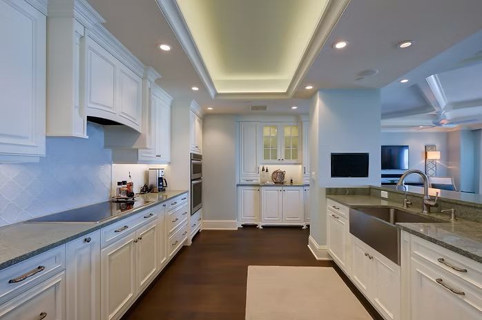 White kitchen with dark wood floors, white cabinets, and stainless steel sink.