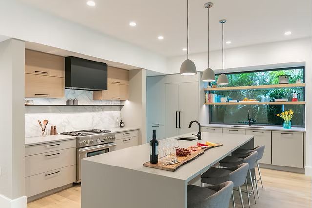 Modern kitchen with gray island, light cabinets, stainless steel appliances, and a window with a green view.