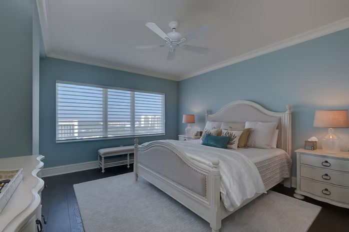 Bedroom with blue walls, white bed and furniture, dark wood floor, and window with blinds.