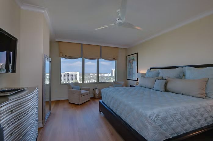 Bedroom with a large bed, windows overlooking a city, and a TV on a dresser.