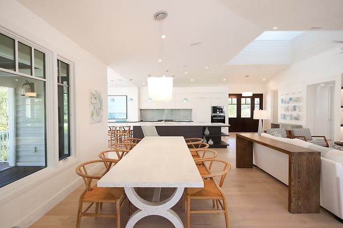 Spacious open-concept dining room with a long table and wooden chairs, leading to a modern kitchen.