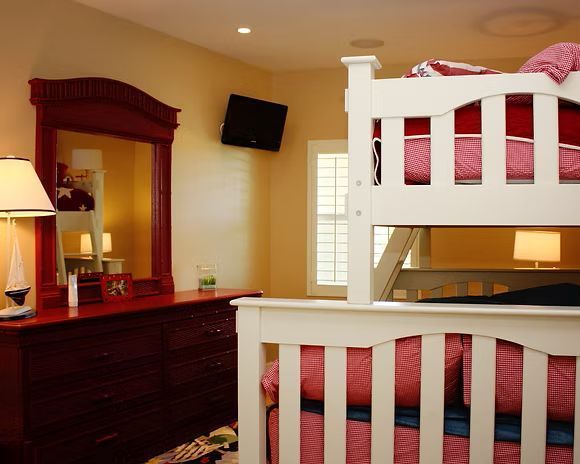 Bedroom with a white bunk bed, a red dresser with a mirror, and a small TV on the wall.
