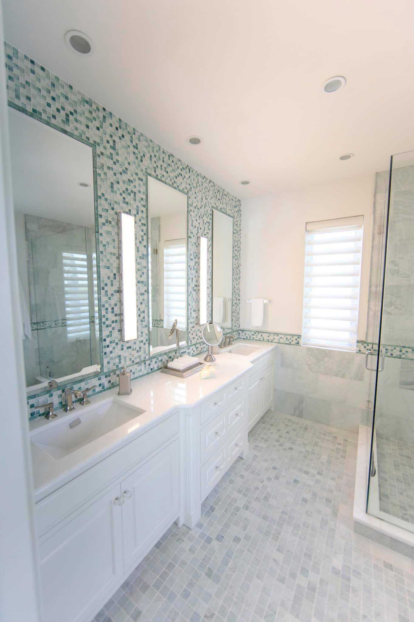 Bathroom with white cabinetry, mosaic tile accent wall, three mirrors, and shower.