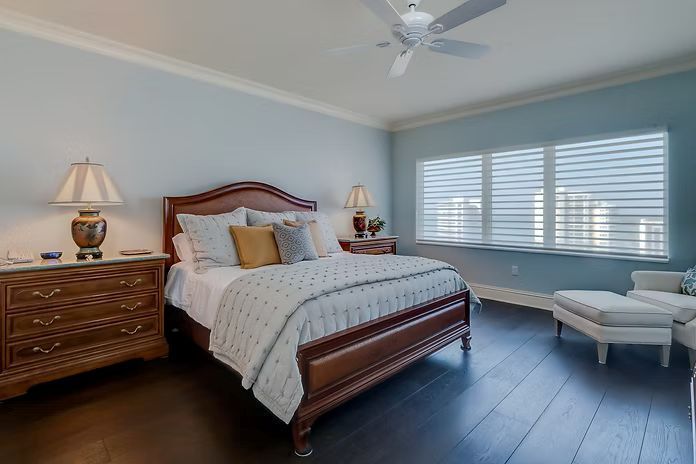 Bedroom with blue walls, dark wood floor, wooden bed frame, nightstands, and a white chair.