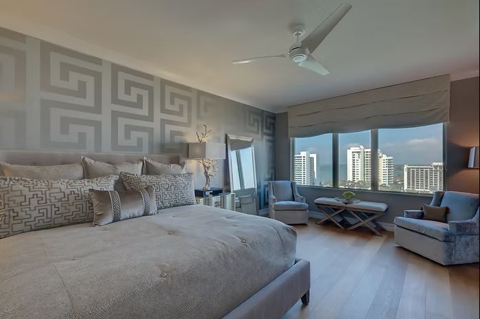 Elegant bedroom with grey geometric wallpaper, bed, chairs, and city view.
