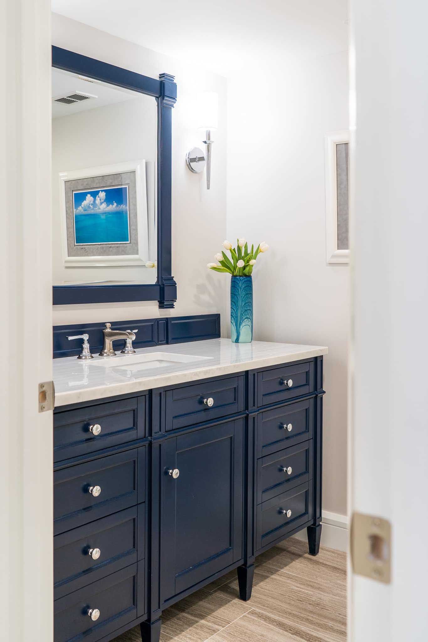 Navy blue vanity in a bathroom with white countertop, chrome fixtures, and floral arrangement.
