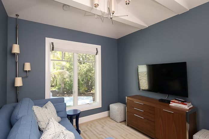 Blue-walled room with window, couch, TV on a wooden dresser, sconces, and a light fixture.