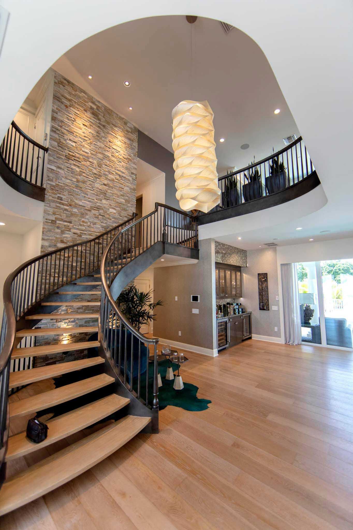 Elegant, curved staircase in a two-story home with light wood floors and stone accent wall.