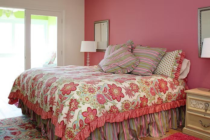 Bedroom with pink walls, floral bedspread, striped bed skirt, and a door leading outside.