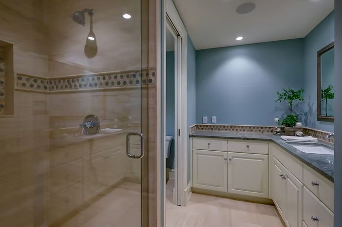 Bathroom with glass shower, blue wall, white cabinets, and granite countertop.