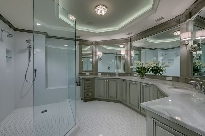 Elegant, gray and white bathroom with a glass shower, double sinks, and vanity mirrors.