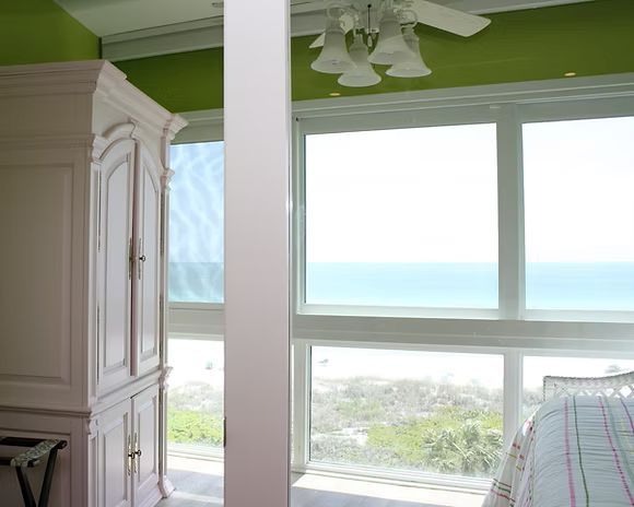 White armoire and pillar in front of large windows with ocean view, green ceiling.