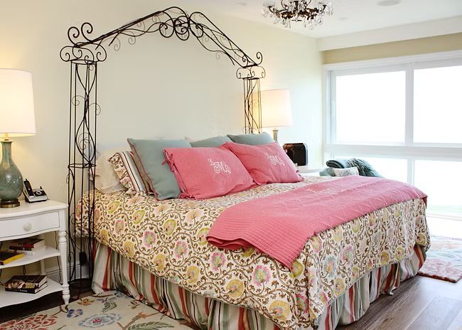 Bedroom with floral bedspread, iron bed arch, two lamps, and a window.