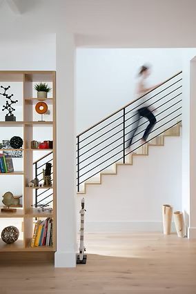 Modern interior with a person blurred on stairs, next to a bookcase, and wooden floors.
