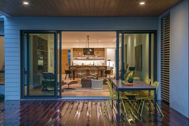 Sliding glass doors open to a modern kitchen and dining area, with a patio featuring a table and chairs.