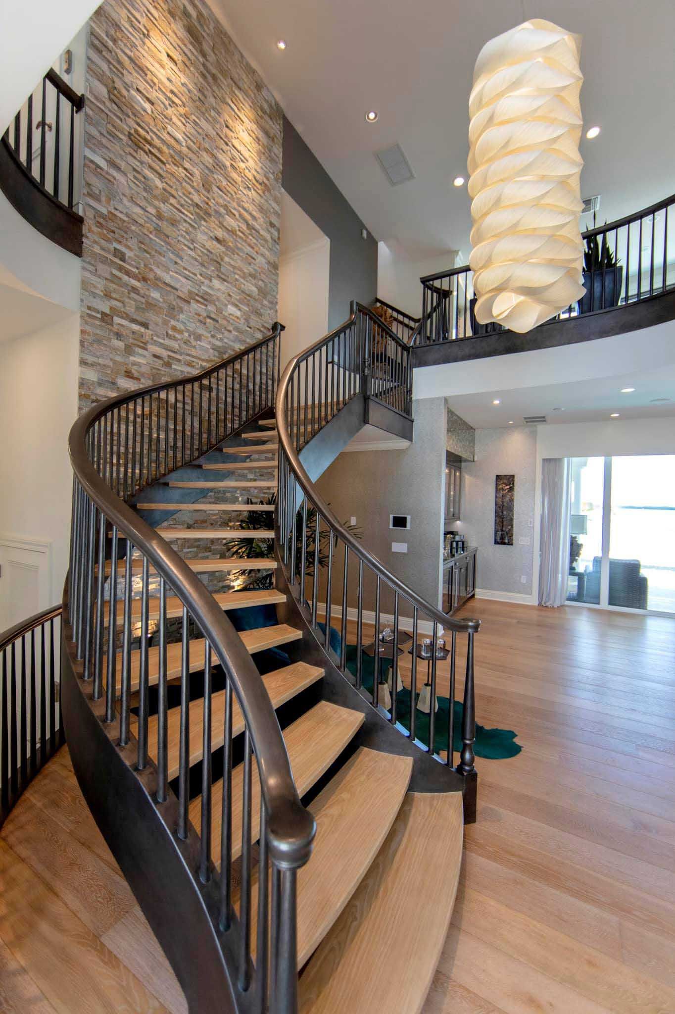 Elegant curved staircase with brown railing and carpeted steps in a two-story home; stone accent wall.