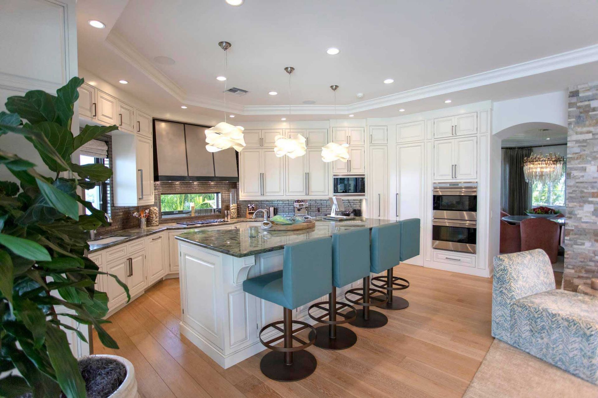 Spacious white kitchen with island, blue stools, and light wood floors.
