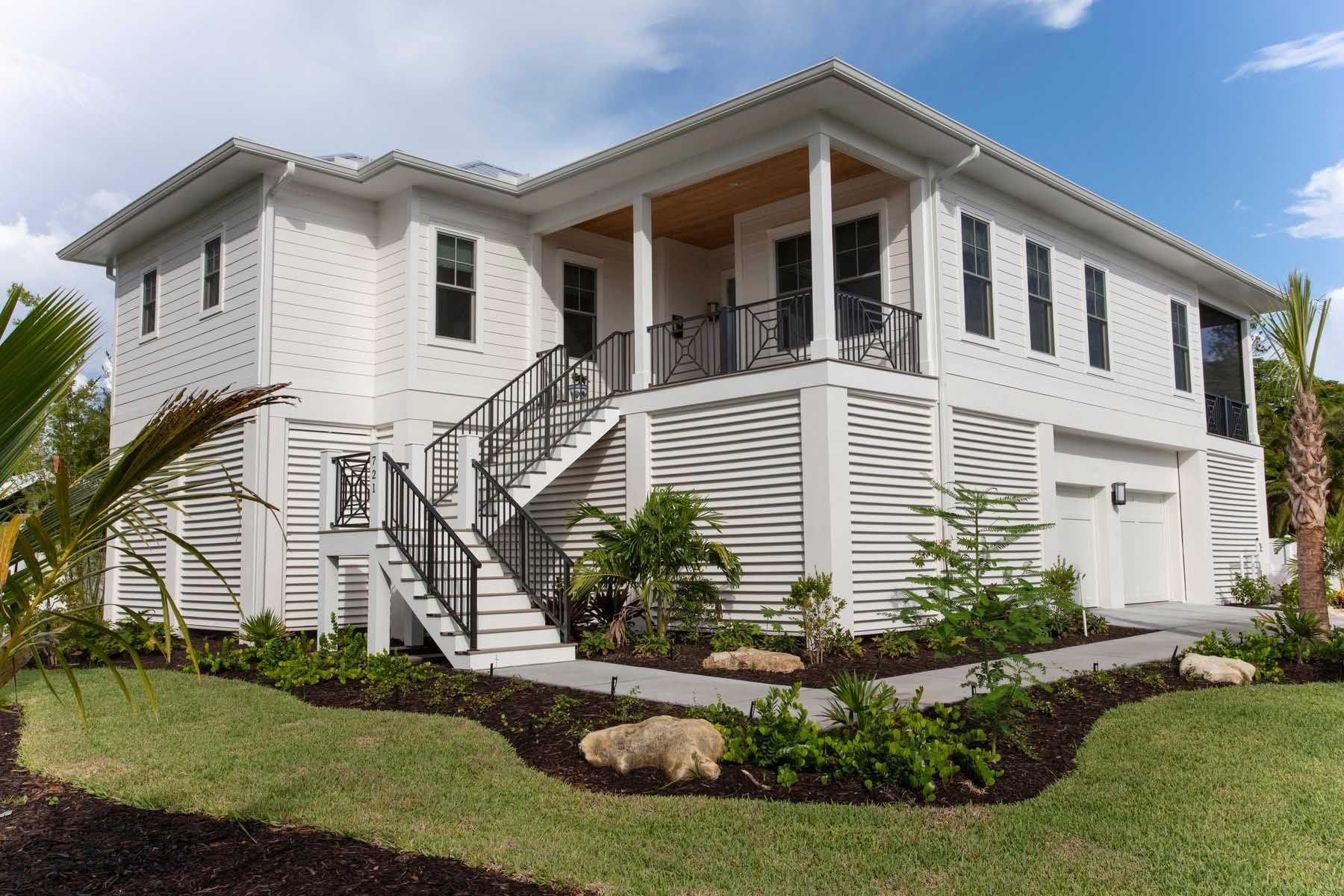 White two-story house with black railing and windows, set on manicured lawn.