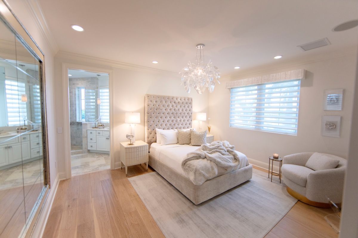 Elegant bedroom with tufted headboard, crystal chandelier, and bathroom doorway.