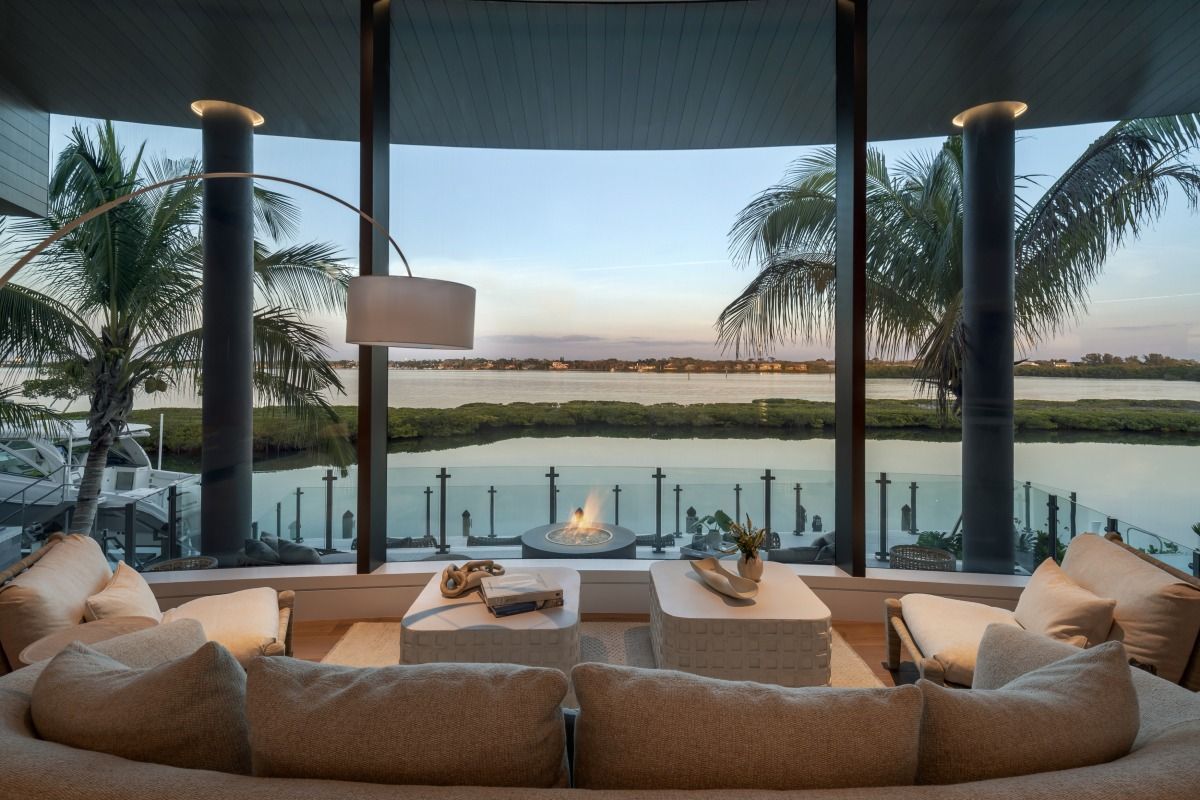 Living room with waterfront view through curved window, white sofas, and palm trees.