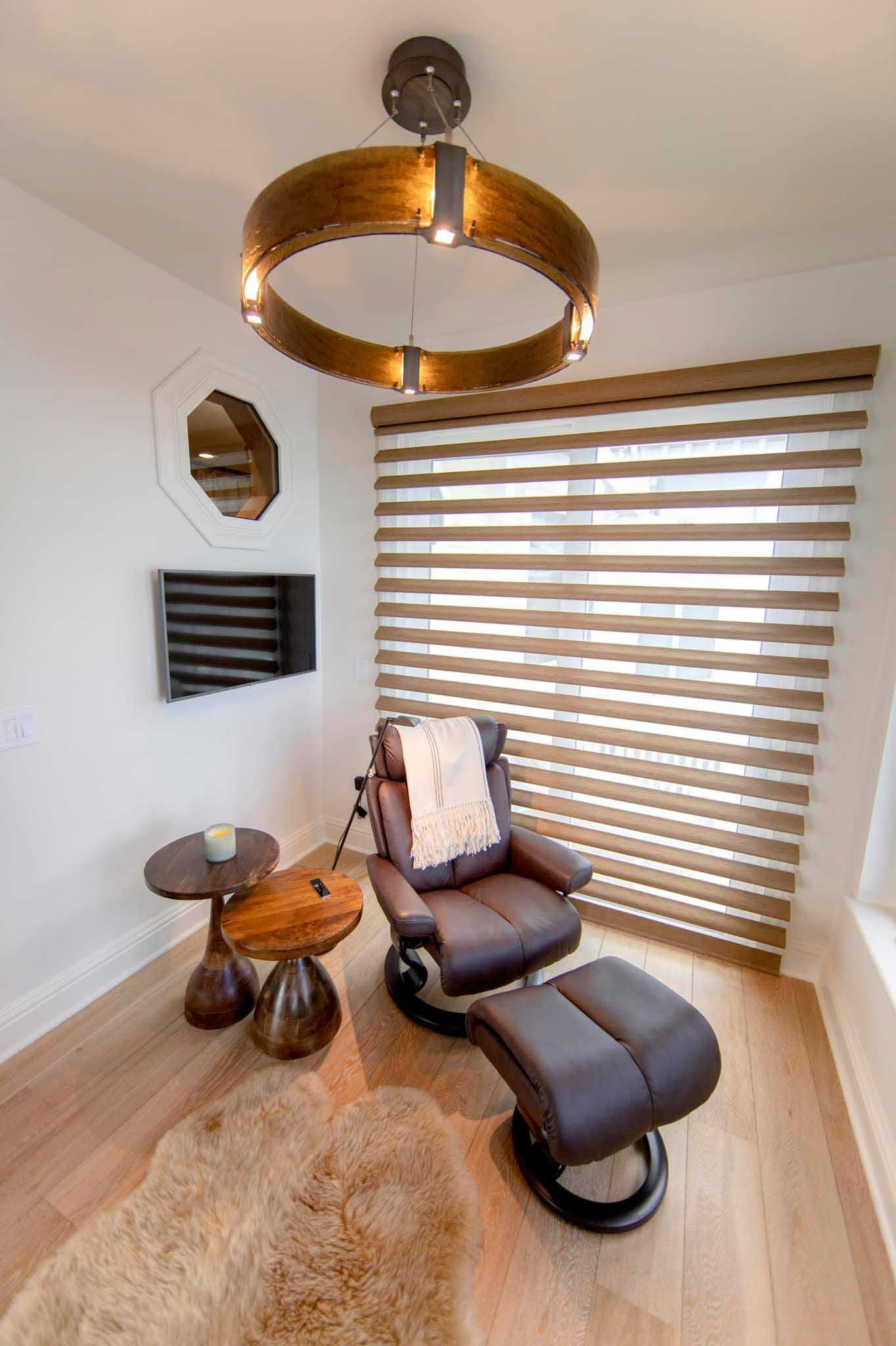 Cozy reading nook with a recliner, ottoman, and round light fixture. Tan and brown hues.